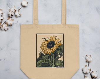 Peut inclure: Un sac fourre-tout beige avec un motif de tournesol imprimé sur le devant. Le tournesol est jaune avec un centre brun foncé et des feuilles vertes. Le texte "Pandora's Tees" est imprimé dans le coin inférieur droit du motif.