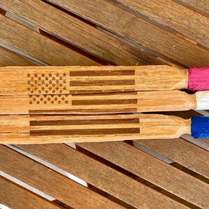 May include: Three wooden sticks with an American flag design painted on them. The ends of the sticks are painted red, white, and blue.