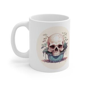 May include: White ceramic mug with a graphic of a skull in a blue pot with plants growing out of it. The text "Kind of Spooky" is printed below the pot.