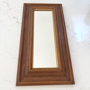 May include: A rectangular wall mirror featuring a thick, dark brown wood-grain frame with a beveled inner edge. The mirror glass is clear and centered within the frame, which displays a prominent vertical wood texture and mitered corners.