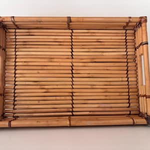 May include: Rectangular bamboo serving tray with built-in handles. The tray is constructed from numerous parallel bamboo rods, creating a textured surface. The frame and handles are made of thicker bamboo, with dark brown accents.
