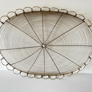 May include: An oval-shaped, antique brass wire basket. The basket features a scalloped edge and a radial wire design emanating from the center. The basket is made of thin, closely spaced wires, creating a delicate yet sturdy structure.