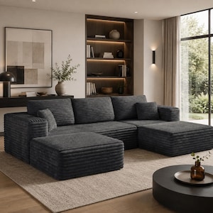 May include: A dark gray corduroy sectional sofa with a matching ottoman, featuring a low-profile design, wide armrests, and thick horizontal ribbed texture. The modular seating arrangement includes three back cushions and two small square throw pillows.
