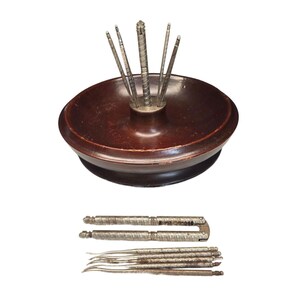 May include: A vintage nutcracker set featuring a dark brown wooden bowl with a central metal holder for picks. The set includes several metal picks and a nutcracker tool, all with a textured design. This antique set is perfect for serving nuts.
