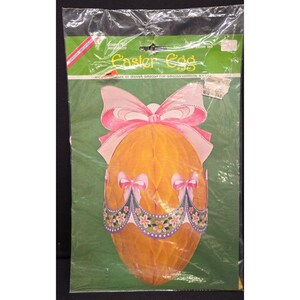 Puede incluir: Una decoración de huevo de Pascua en un paquete de plástico. El huevo es naranja con lazos rosas y un diseño floral. El paquete tiene las palabras "Easter Egg" y un fondo verde.