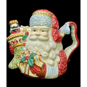 May include: A ceramic Santa Claus teapot with a white beard, blue eyes, and a red hat. The teapot features a handle and spout, and is decorated with gifts and a nutcracker. The teapot is a festive holiday decoration.