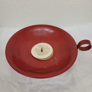 Könnte beinhalten: Roter Kerzenhalter aus Metall mit einem Griff. Der Halter hat einen weißen Papierkreis in der Mitte mit den Worten "Wond'r-Glo" und Anweisungen zur Verwendung der Kerze.
