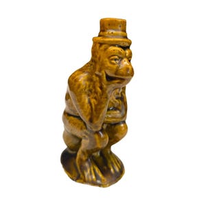 Pode incluir: Estatueta de cerâmica marrom de um macaco usando uma cartola. O acabamento brilhante destaca os detalhes do macaco. A estatueta está em uma pose agachada, dando-lhe uma aparência vintage e caprichosa.
