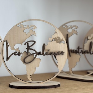 Peut inclure: Décorations en bois en forme de globe terrestre, avec des continents découpés et le mot "Les Baléares" en écriture cursive. Les globes sont posés sur des socles en bois.