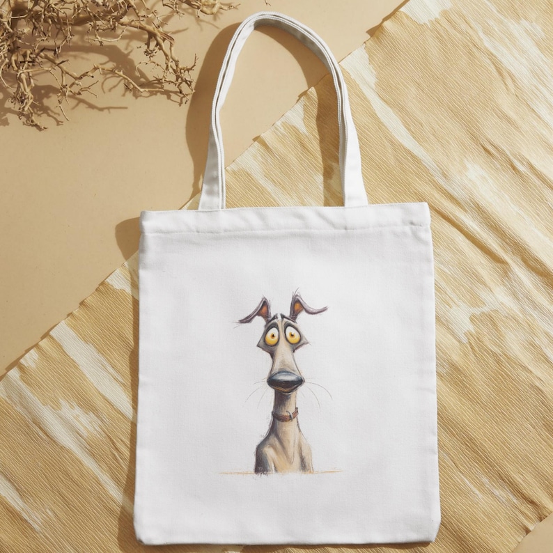 May include: White tote bag featuring a whimsical illustration of a dog with large, expressive eyes and a long snout. The dog is depicted in shades of gray and tan, with a red collar. The bag has white handles.