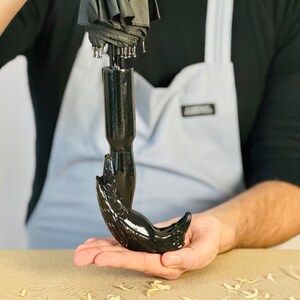 May include: A black umbrella with a unique handle shaped like a hand. The handle is made of a smooth, black material and has a detailed design.