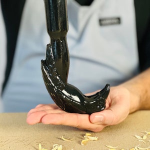 May include: A black, hand-shaped bottle opener with a shiny, glossy finish. The opener is being held in a person's hand.