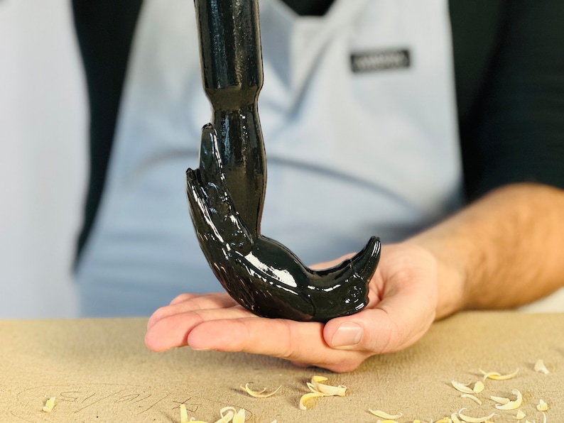 May include: A black, hand-shaped bottle opener with a shiny, glossy finish. The opener is being held in a person's hand.