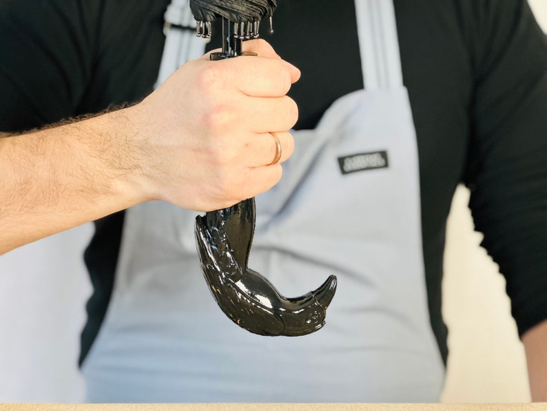 May include: A black umbrella with a bird-shaped handle. The handle is made of a smooth, black material and has a detailed design.