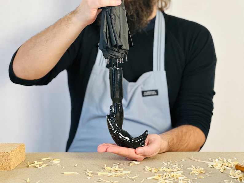 May include: A black umbrella with a unique, hand-shaped handle. The handle is made of a smooth, black material and resembles a human hand.