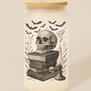 May include: A frosted glass tumbler with a bamboo lid and straw. The tumbler features a black and white illustration of a skull, books, bats, and a lamp. The text "Custom Name on Lid" is above the tumbler.