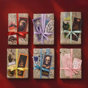 Puede incluir: Seis regalos envueltos sobre una superficie roja. Los regalos están envueltos en papel de periódico y atados con cintas de varios colores. Cada regalo está decorado con una pegatina o tarjeta diferente.