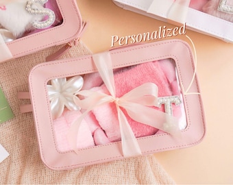 Puede incluir: Juego de regalo rosa en una caja con ventana transparente, atado con una cinta. El juego incluye un artículo rosa esponjoso, una flor blanca y la letra "T" adornada con perlas. La palabra "Personalizado" está escrita en la imagen.