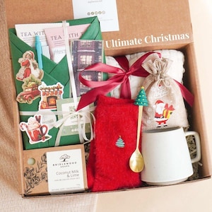 Puede incluir: Una caja de regalo navideña llena de artículos festivos. Incluye una taza blanca, un calcetín rojo, una cuchara decorativa, sobres de té, jabón y una pequeña bolsa con un diseño de Papá Noel. La caja está etiquetada como "Ultimate Christmas".