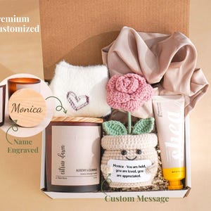 May include: A gift box with a candle, a crocheted flower, a cream, a plush item with a heart, and a custom message. The candle has a wooden lid engraved with a name. The box is labeled "Premium Customized".