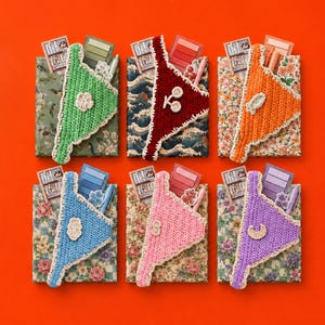 May include: Six rectangular notebooks with patterned covers, each featuring a triangular crochet pocket in green, dark red, orange, blue, pink, or purple. Each pocket holds a small card, a colour swatch strip, a pen, and a small crochet applique.
