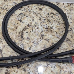 May include: Black audio cable with RCA and XLR connectors. The cable is coiled in a circular shape and lies on a speckled surface. The connectors have red and silver accents.