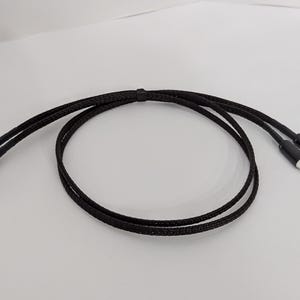 May include: A black audio cable with two RCA connectors. The cable is braided and has a red accent on the connectors.