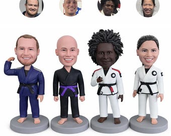 May include: Four bobblehead figures of people in martial arts uniforms. The figures are on gray bases and have smiling faces. The uniforms are in various colors, including blue, black, and white, with black belts. Above the figures are four headshots.