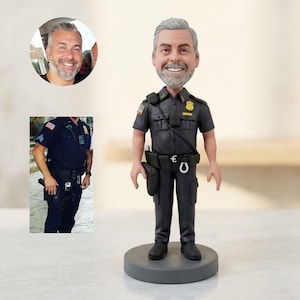 May include: A custom bobblehead figurine of a police officer in a dark uniform, complete with a badge, radio, and utility belt. The figure has a smiling face with gray hair and a beard, standing on a gray circular base. Two smaller images are in the background.