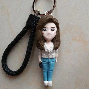 May include: A brown haired woman with a white shirt and blue jeans is attached to a black leather keychain with a silver ring.
