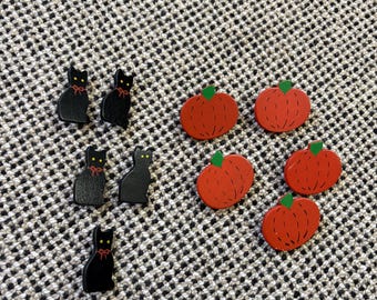 May include: A collection of small flat decorative pieces including five black cat shapes with yellow eyes and red bow details, and four orange pumpkin shapes with green stems and black line accents, arranged on a textured gray surface.