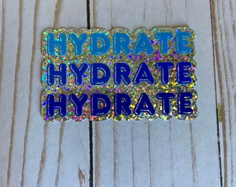 May include: A gold glitter sticker with the word "HYDRATE" repeated three times in blue and black letters.