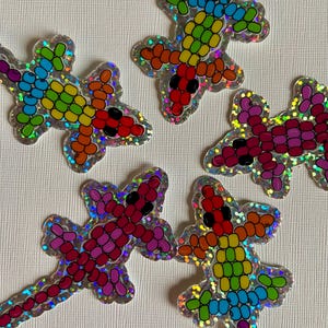 May include: Five iridescent rainbow colored lizard stickers. Each lizard is made of small, round, colorful beads. The lizards are arranged in a star shape on a white background.