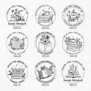 May include: Nine black and white circular rubber stamps with different designs featuring books, flowers, and coffee cups. Each stamp has text that reads "From the Library of" and a name below. The text "EEA-25" through "EEA-33" is below each stamp.