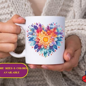 May include: White ceramic mug with a colorful floral design in the shape of a heart. The design features shades of blue, purple, pink, orange, and yellow. The text "MORE SIZES & COLORS AVAILABLE" is printed below the design.