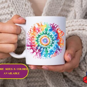 Op de afbeelding: Een witte keramische mok met een kleurrijk mandala-ontwerp. De mandala heeft een regenboog van kleuren, waaronder rood, oranje, geel, groen, blauw, indigo en violet. De mok heeft een handvat en wordt vastgehouden door een hand.
