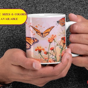 May include: White ceramic mug with a colorful design of butterflies and flowers. The butterflies are orange and black with white spots. The flowers are orange and yellow. The mug has a handle on the right side.