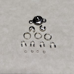 May include: A set of silver-toned jewelry making supplies, including a clasp, jump rings, crimp beads, and end caps.