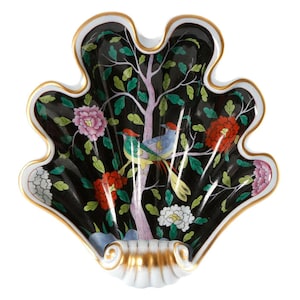May include: A black porcelain shell-shaped dish with a gold rim. The dish is decorated with a colorful floral and bird design. The birds are perched on a tree branch with pink flowers and green leaves.