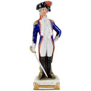 Puede incluir: Figura de porcelana de un hombre con uniforme militar azul con detalles dorados, calzones blancos y botas negras. Lleva un sombrero tricornio con una pluma y sostiene una espada. La base dice "LA FAYETTE".