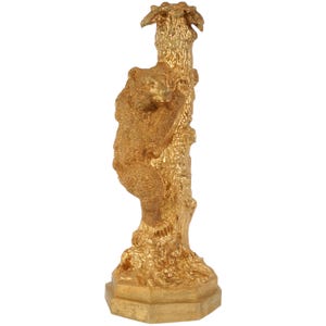 May include: A gold-toned metal sculpture of a bear climbing a tree. The sculpture is detailed and has a textured finish.