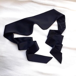 Puede incluir: Una máscara para dormir de satén negro con una banda ancha que se ata en la parte posterior de la cabeza.