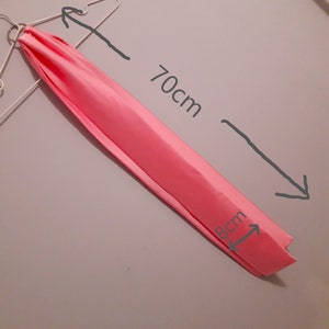 Puede incluir: Una bufanda de tela rosa que mide 70 cm de largo y 8 cm de ancho.