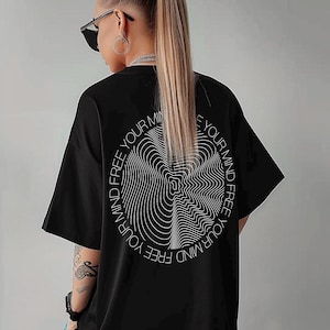 May include: Black oversized t-shirt with a white circular graphic on the back. The graphic features a wavy design and the text "FREE YOUR MIND" around the perimeter. The shirt has short sleeves and a relaxed fit.