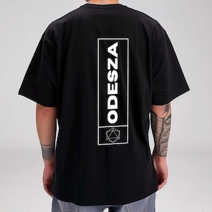 May include: Black t-shirt with a white graphic of the word "ODESZA" and a geometric design.