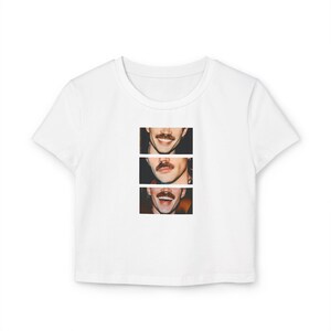 Puede incluir: Top corto blanco con un gr&aacute;fico de tres caras sonrientes con bigotes. Las caras est&aacute;n dispuestas verticalmente, cada una con una expresi&oacute;n diferente. La camiseta est&aacute; hecha de un material suave y ligero.