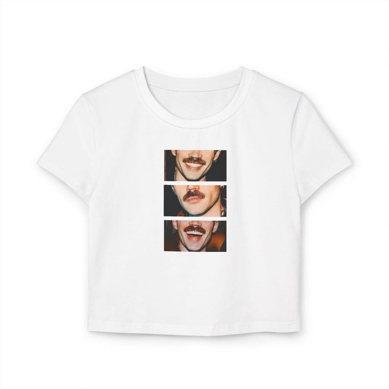 Puede incluir: Top corto blanco con un gr&aacute;fico de tres caras sonrientes con bigotes. Las caras est&aacute;n dispuestas verticalmente, cada una con una expresi&oacute;n diferente. La camiseta est&aacute; hecha de un material suave y ligero.