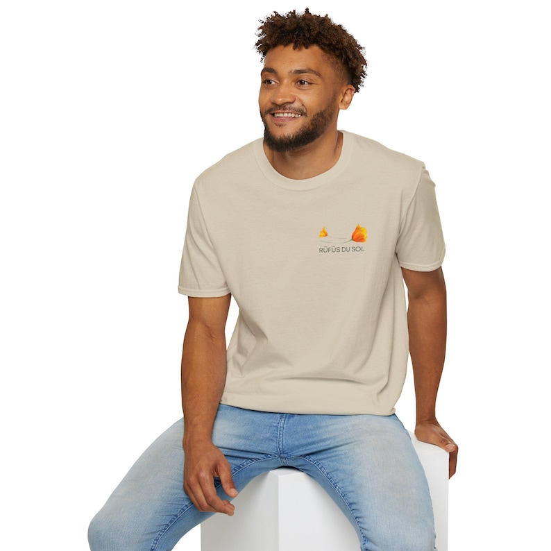 May include: A beige t-shirt with a small orange and yellow graphic of a flower and the text "Rufus du Sol" on the front.