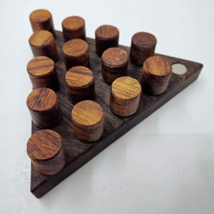 May include: A wooden triangular game board with 15 wooden cylinders arranged in a pyramid shape. The board has a small, round, white magnet in the top corner.