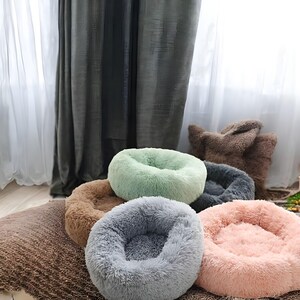 以下が含まれることがあります： 緑、茶色、灰色、ピンクなど、さまざまな色のふわふわしたペットベッドが5つあります。ベッドはすべてドーナツ型で、柔らかくふわふわした質感です。